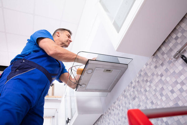 Elevated View Of Male Technician Checking Extractor Filter With Digital Multimeter In Kitchen