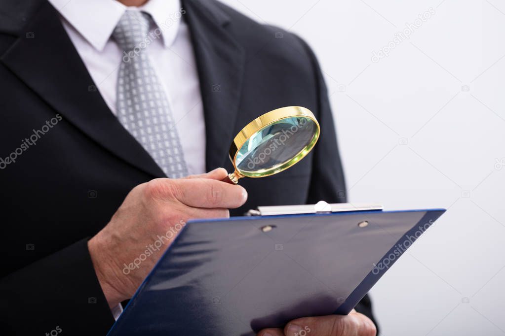 Close-up Of  Businessman Analyzing Document  Through Magnifying Glass At Workplace