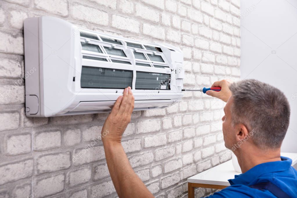 Mature Male Technician Fixing Air Conditioner With Screwdriver