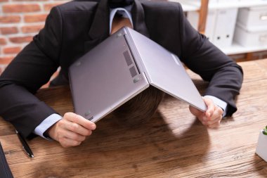 A Businessman Covering His Head With Laptop Over The Desk At Workplace clipart