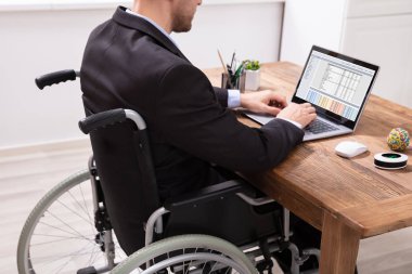 İşyerinde dizüstü kullanarak tekerlekli sandalye üzerinde oturan Engelli iş adamı