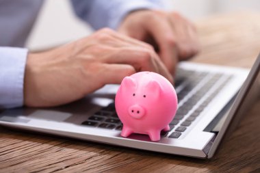 Business sperson 's Hand Pembe Piggybank ile Dizüstü bilgisayarda çalışıyor