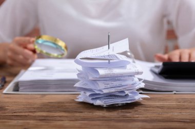 Hesap Makinesi ve Büyüteç kullanarak Faturaları Hesaplayan Bir Kişi Önünde Faturalar