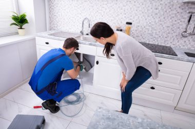 Erkek Tesisatçıya Bakan Kadın Mutfakta kurutulmuş kabloyla tıkanmış lavabo borusunu temizliyor