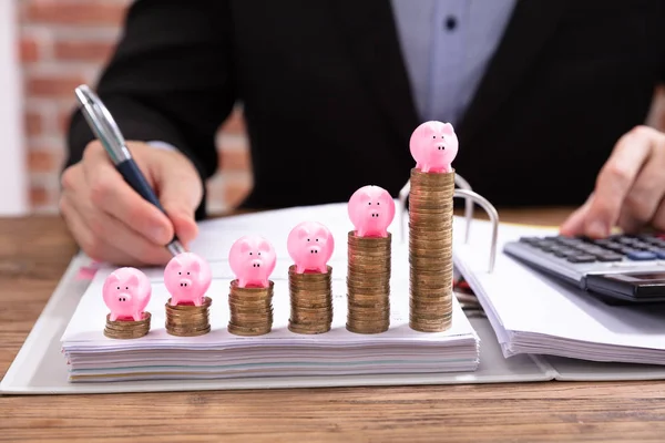 Pink Piggybank Over Stacked Coins In Front Of Businessman Calculating Invoice