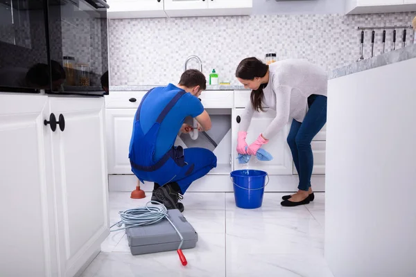 若い女性の男性配管工の台所シンクのパイプを修復しながらの床のクリーニング — ストック写真