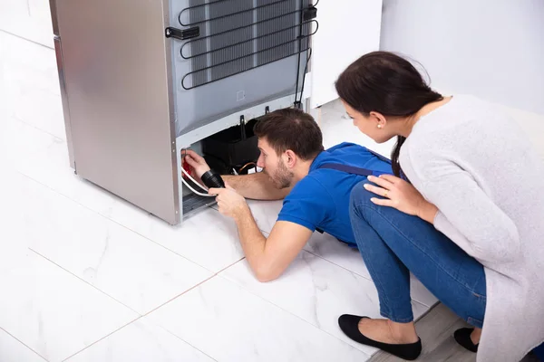快乐的女人看着技师用荧光灯检查厨房里的冰箱 — 图库照片