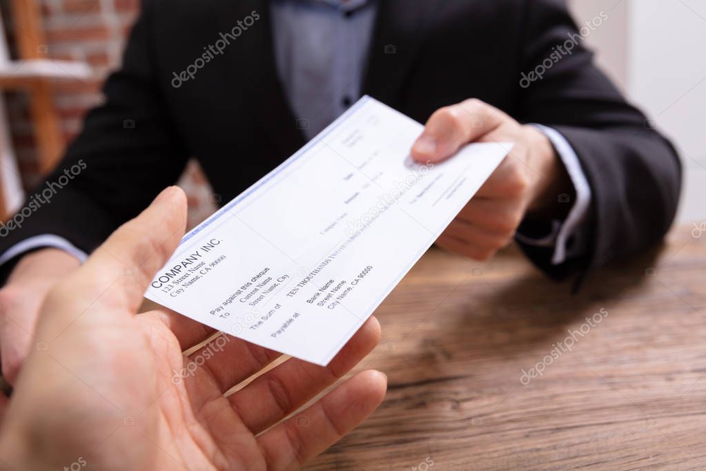 Close-up Of Businessman's Hands Giving Cheque To Other Person In Office