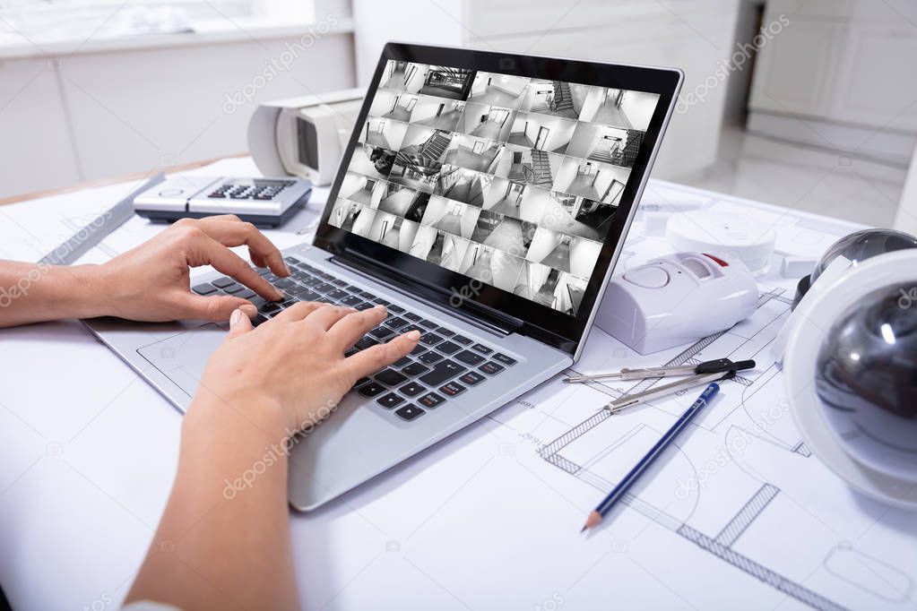 Close-up Of A Woman Monitoring Home Security Cameras On Laptop Over The Blue Print
