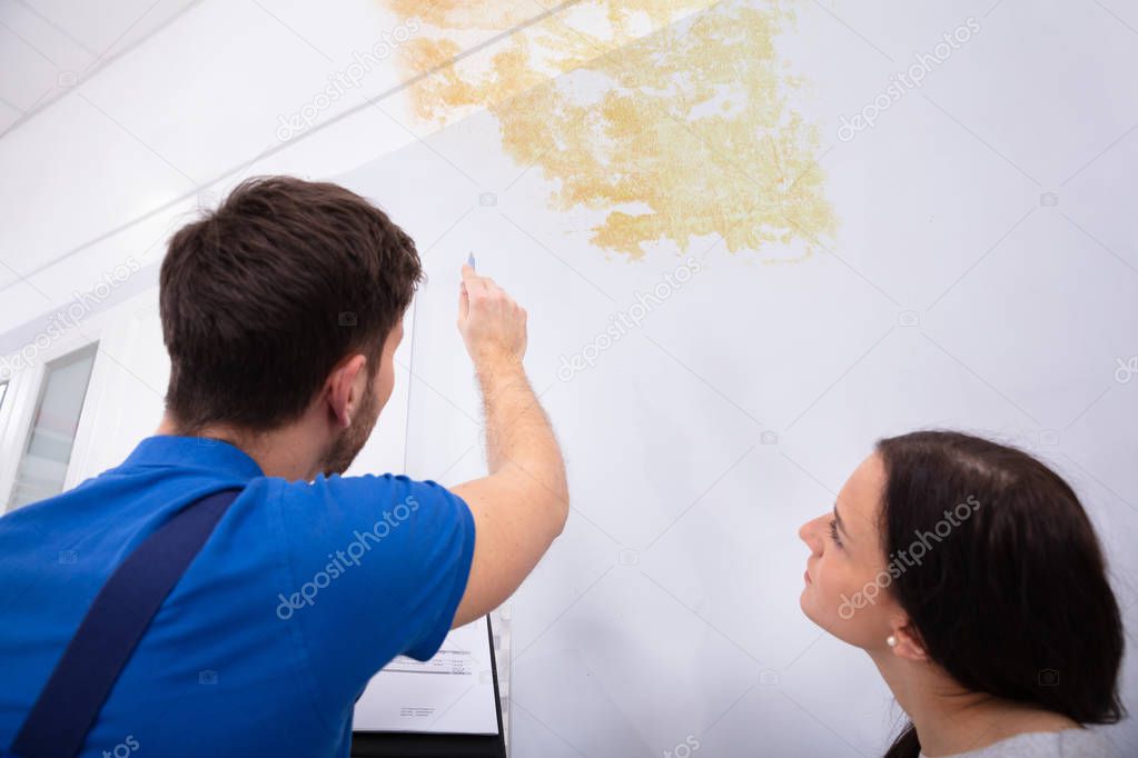 Young Worker Writing On Clipboard With Woman Standing In Kitchen