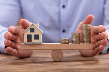 Küçük ev modeli ve yığılmış altın sikke üzerinde ahşap tahterevalli Dengeleme