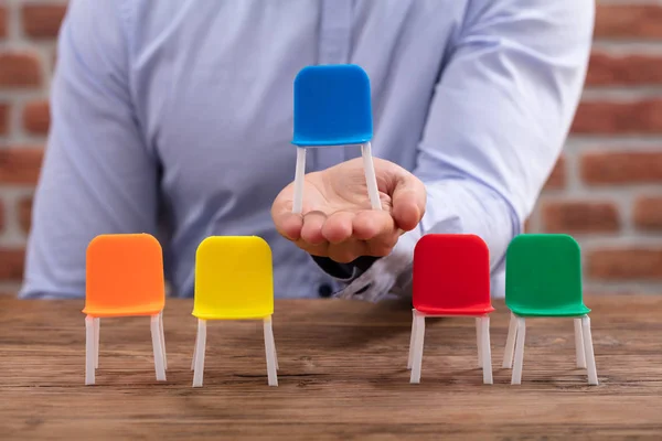 Person Hält Blauen Stuhl Neben Bunten Stühlen Auf Dem Schreibtisch — Stockfoto