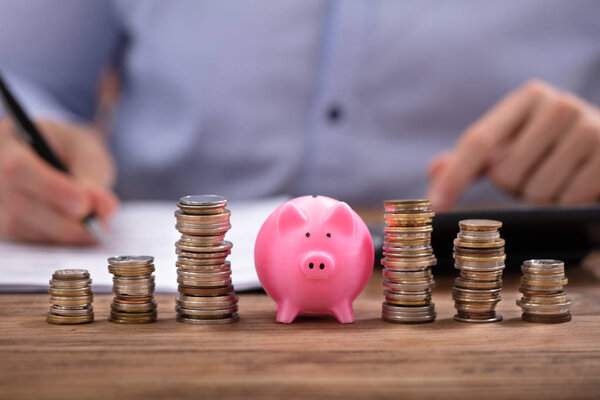 Упакованные монеты и розовый поросенок банк перед бизнесменом расчета счета на деревянном столе
