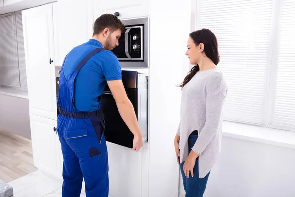 Mooie Vrouw Kijken Naar Jonge Serviceman Installeren Oven Keuken — Stockfoto