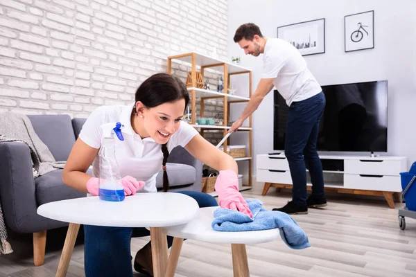 Dwóch Uśmiechniętych Młodych Pracowników Sprzątających Stół Wycierających Podłogę Salonie — Zdjęcie stockowe