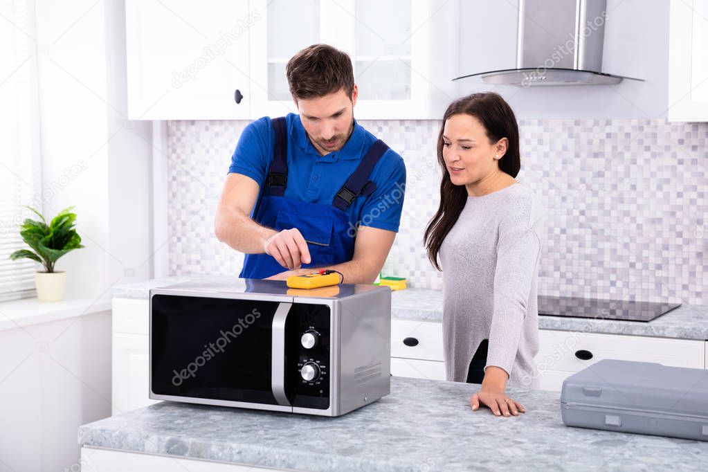 Pretty Woman Standing Near Repairman Repairing Oven Using Digital Multimeter In Kitchen