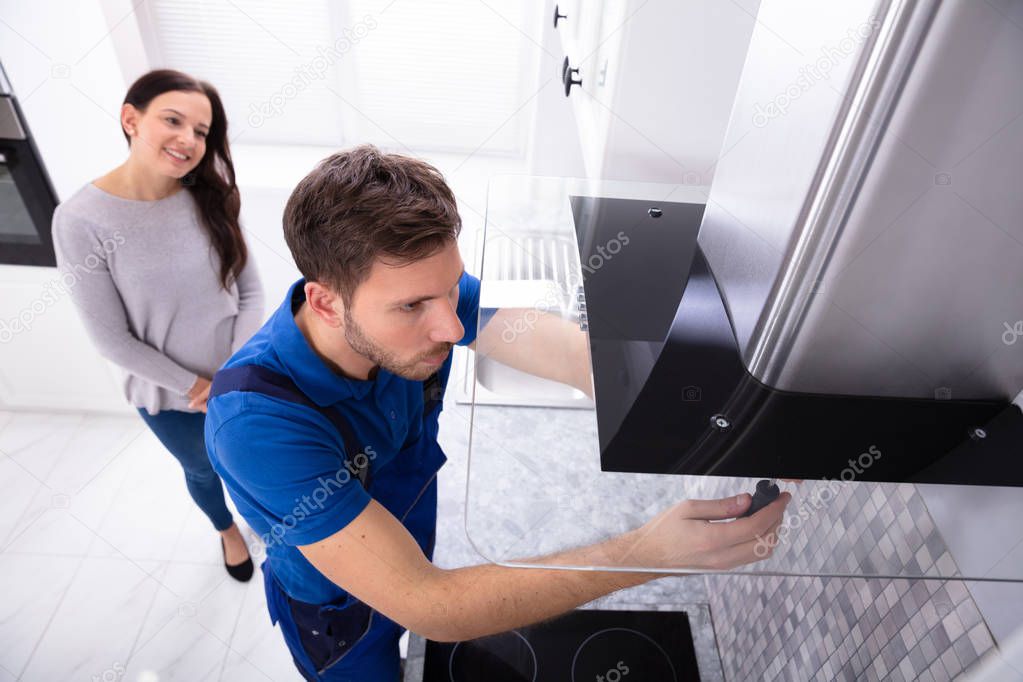 Smiling Woman Standing In Front Of Male Worker Fixing Kitchen Hood With Screwdriver