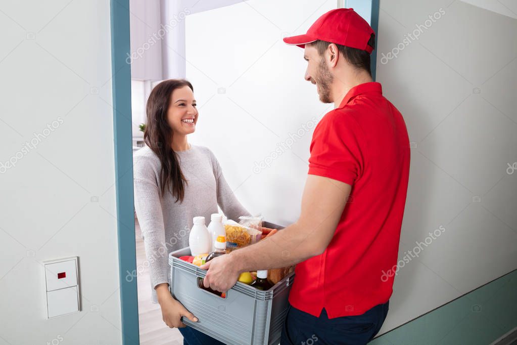 Smiling Young Woman Accepting Full Of Groceries From Delivery Man