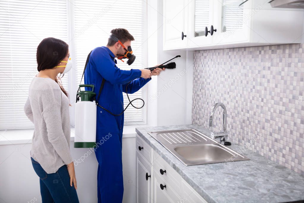 Pest Control Worker And Woman Spraying Pesticide With Torch In Kitchen
