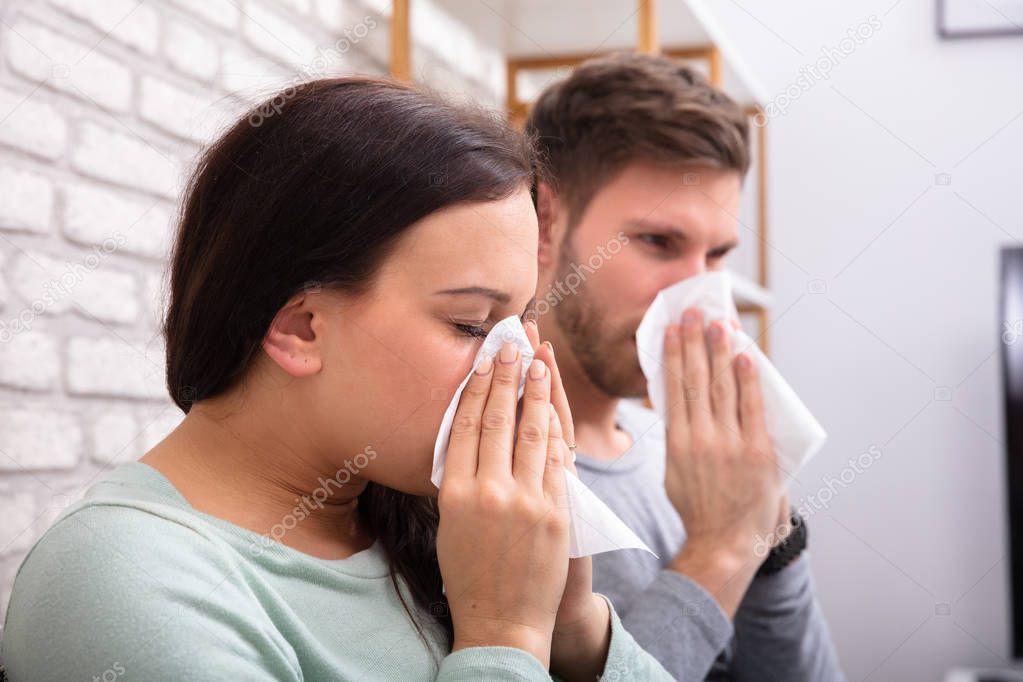 Close-up Of Sick Couple Sneezing In Tissue At Home