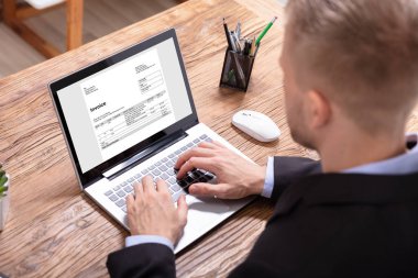 Close-up Of A Businessman's Hand Checking Invoice On Laptop clipart