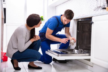 Genç kadın erkek tamirci mutfakta bulaşık makinesi tamir bakarak