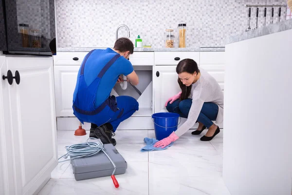 年轻女子清洁地板 而男性水管工修复水槽管在厨房 — 图库照片