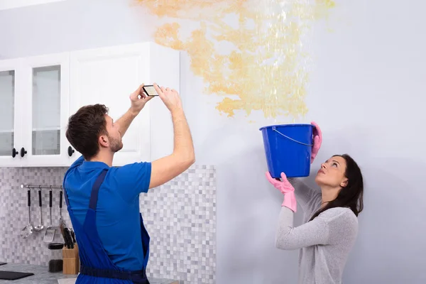 Mulher Coletando Água Balde Azul Teto Danificado Enquanto Reparador Tirando — Fotografia de Stock