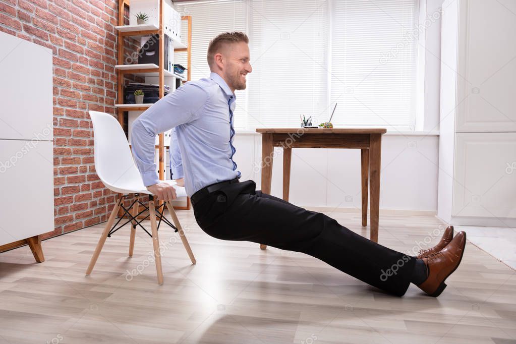 Happy Young Businessman Doing Triceps Dips In Office