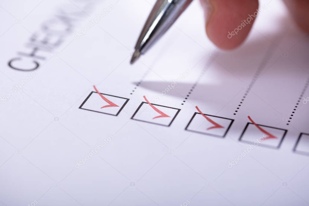 Close-up Of Person's Hand Marking On Checklist With Pen