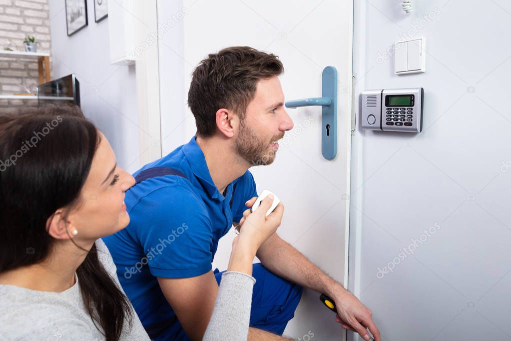 Close-up Of Handyman Installing Security System Near Door Wall While Woman Using Remote