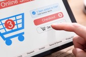 Die Hand der Person beim Online-Shopping auf dem Tablet mit dem Einkaufswagen auf dem Bildschirm