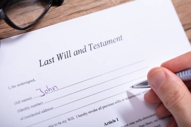 Close-up Of A Person's Hand Filling Last Will And Testament Form