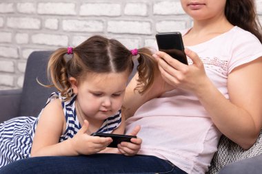 Anne ve kızı koltukta oturan ve evde Mobilephone kullanarak yakın çekim