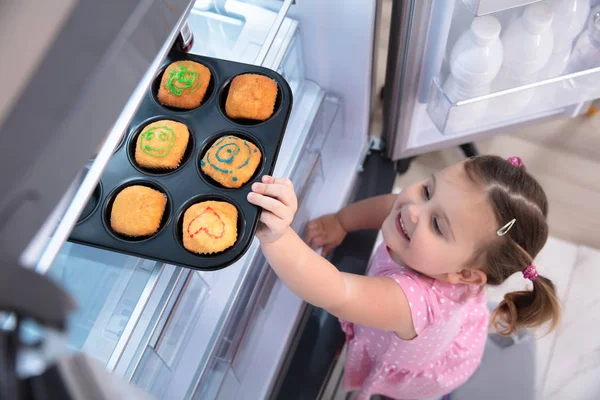 Милая Маленькая Девочка Пытается Протянуть Руку Забрать Кексы Холодильника Дома — стоковое фото