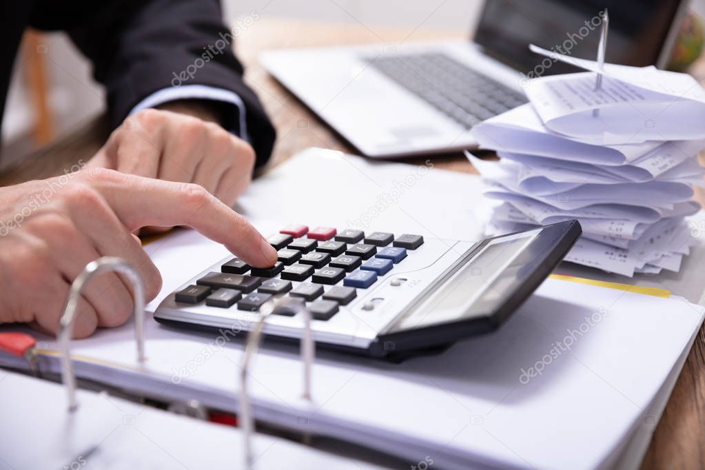 Close-up Of Businessman's Hand Using Calculator While Calculating Invoice On Desk