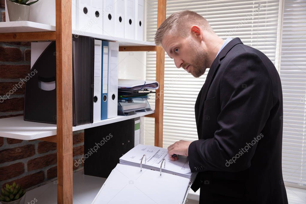 Close-up Of A Businessman Examining The Invoice Document Secretly In Office