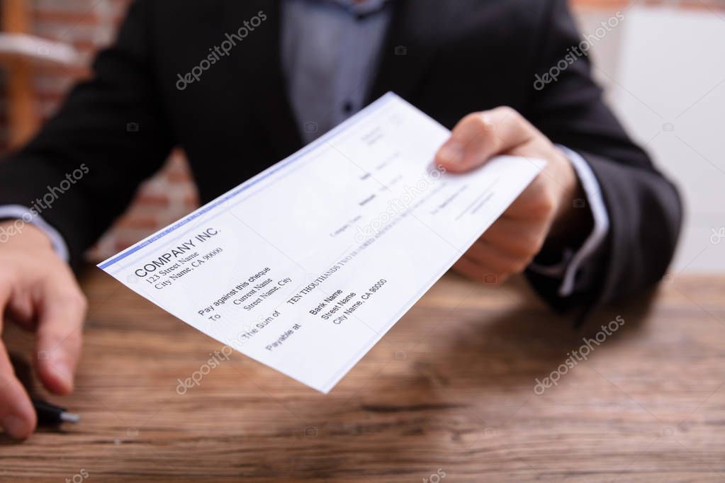 Mid-section Of Person Giving Cheque Over Wooden Desk