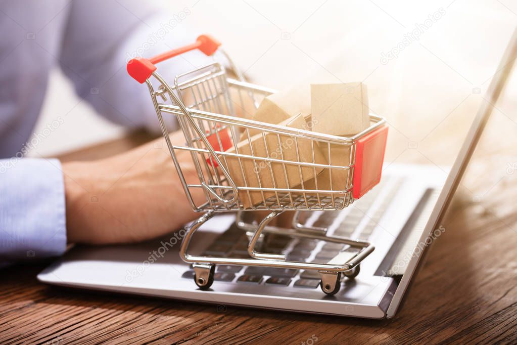 Close-up Of Man Using Laptop With Miniature Cardboard Boxes In The Shopping Trolley