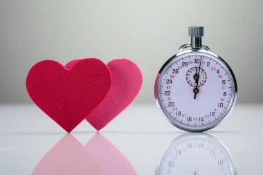 Kırmızı ve pembe kalp şekli ile kronometre beyaz masa üzerinde yansıması