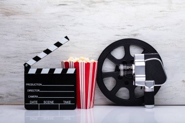 Close-up Of An Movie Camera With Popcorn And Clapper Board Against White Background clipart