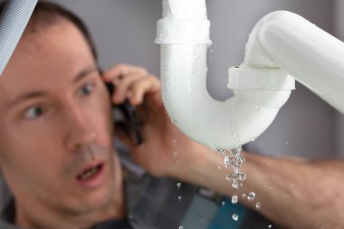 Şok olmuş genç adam mutfaktaki lavabo borusunu tamir etmek için tesisatçıyı arıyor.