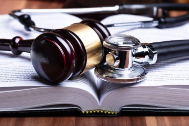 Stethoscope ve tokmağın ahşap masanın üzerindeki açık hukuk kitabının yakın çekimi