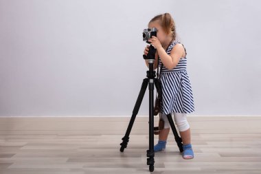 Yerde duran küçük masum kız kameralı ve tripodlu fotoğraf çekiyor.