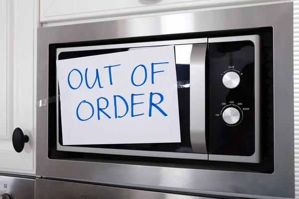 Written Text Out Of Order Message On Paper Over The Stuck Microwave Oven In Kitchen