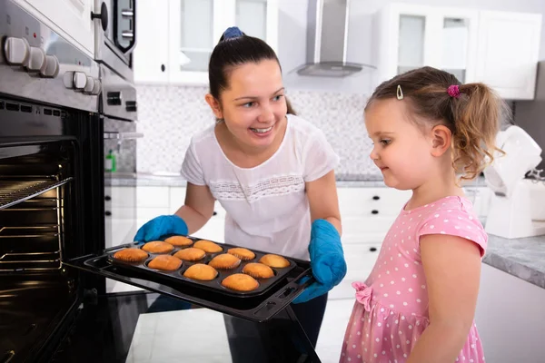 Giovane Madre Holding Cupcake Vassoio Mentre Guardando Suo Figlia Cucina — Foto Stock