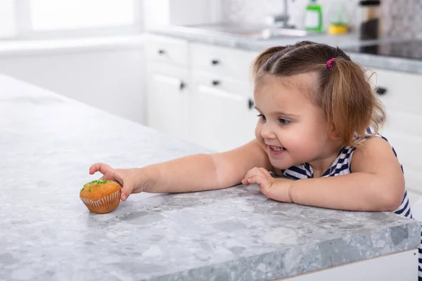 Smiling Cute Girl\'s Hand Reaching For Cupcake On Kitchen Counter