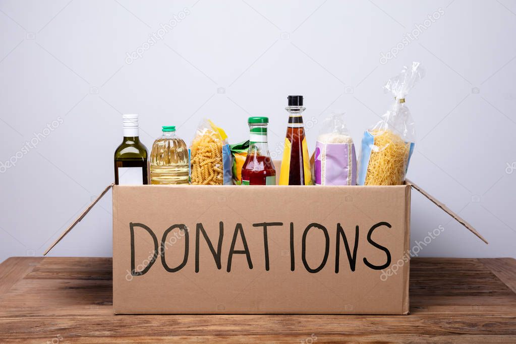 Close-up Of A Donation Box With Various Food Items On Wooden Desk