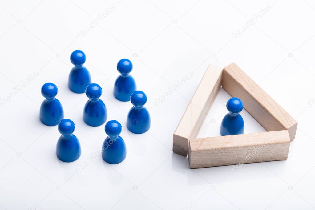 Close-up Of Figurine Pawn Separated By Wooden Blocks From Blue Figurines Over White Background