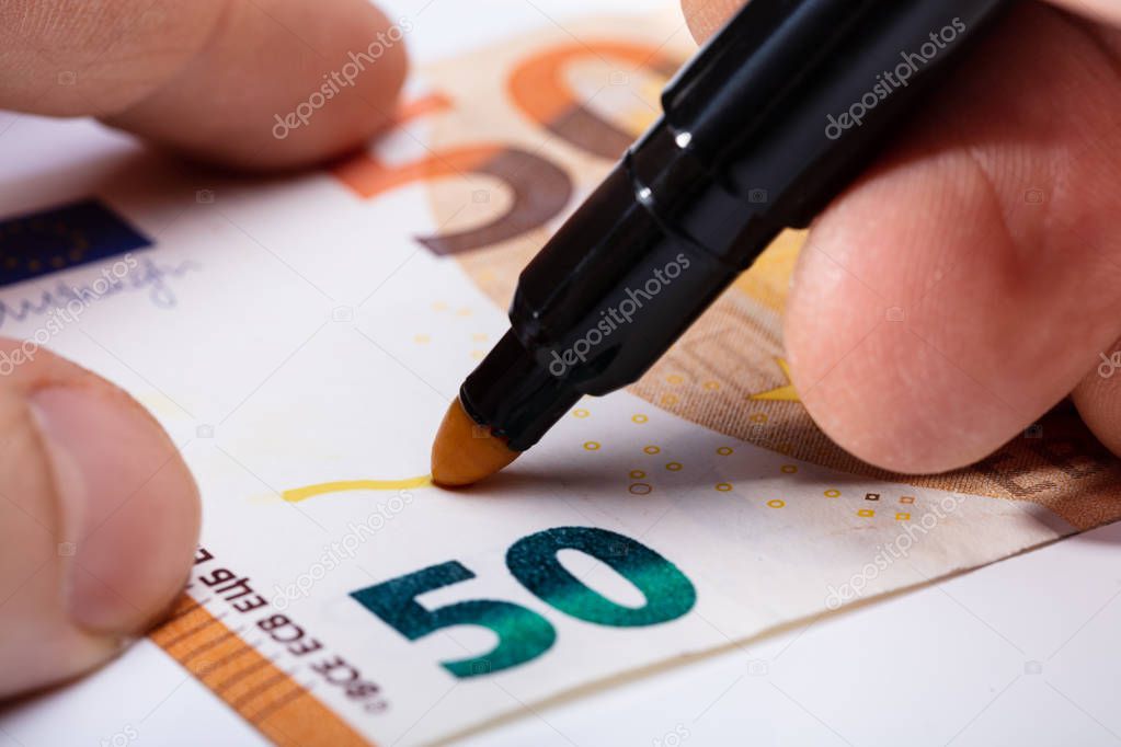 Close-up Of Hand Writing On Banknote With Yellow Marker